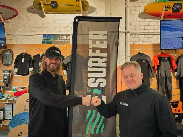 Wayne and Andreas fist bumping each other in front of an E-Surfer banner in front of the Blua Blue surf shop.